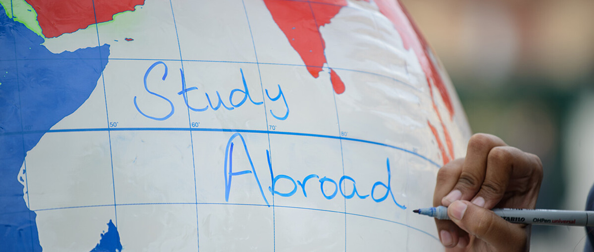 Eine Hand schreibt die Worte "Study abroad" auf einen aufgeblasenen Globus