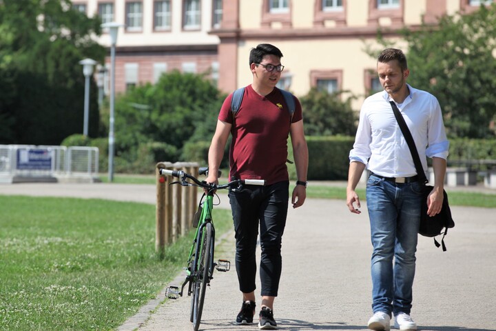Studierende laufen über Mensa Wiese, ein Student schiebt ein Fahrrad