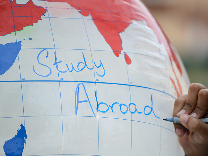 Eine Hand schreibt "Study Abroad" auf einen aufgeblasenen Globus