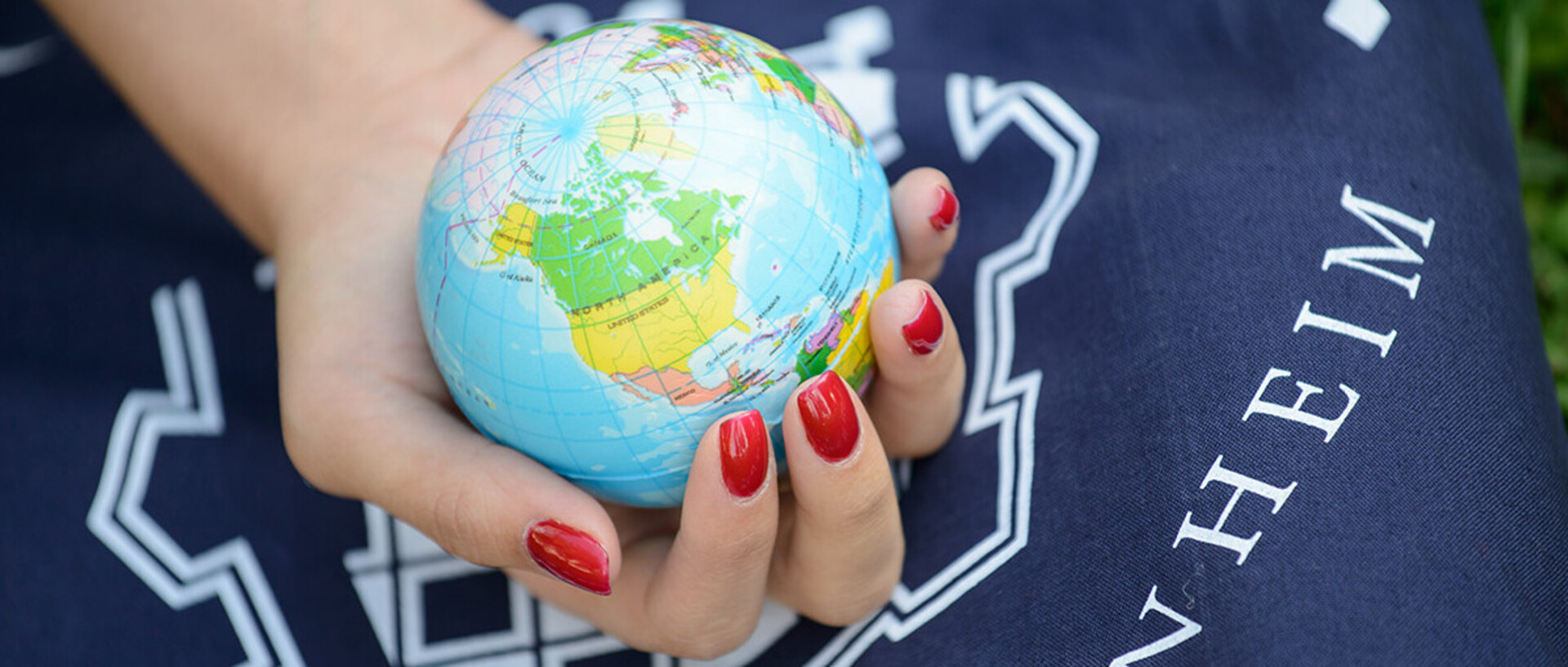 Eine Hand mit rot lackierten Fingernägeln hält einen Globus