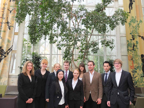 Gruppe von Studierender in formeller Kleidung vor  einem großen Fenster mit Pflanze