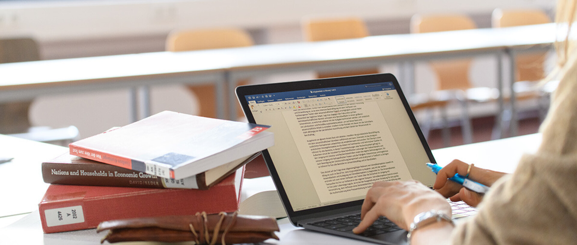 Eine Frau schreibt auf ihrem Laptop in einem Word-Dokument, daneben liegen einige Bücher.