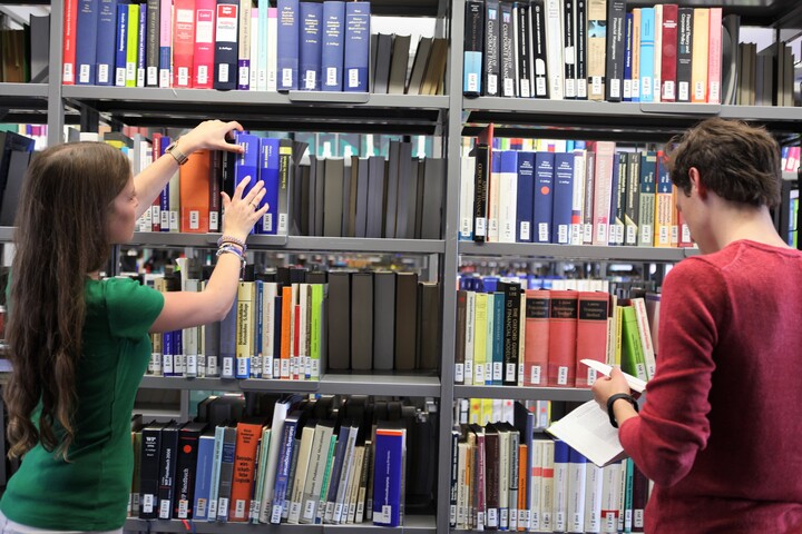 Zwei Studierende stehen vor einem Bücherregal