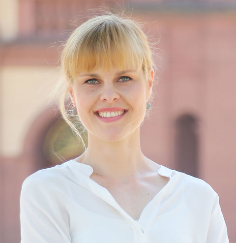 Lea Tochtermann in white blouse outside palace, smiling into camera