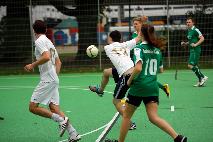Frauen und Männer auf einem Fußballplatz am Fußballspielen. Die Personen tragen grüne und weiße Trikots.