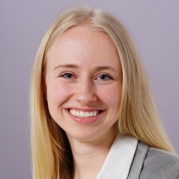 Porträt von Alena Lennartz. Sie trägt ein graues Sakko, dazu ein weißes Hemd.