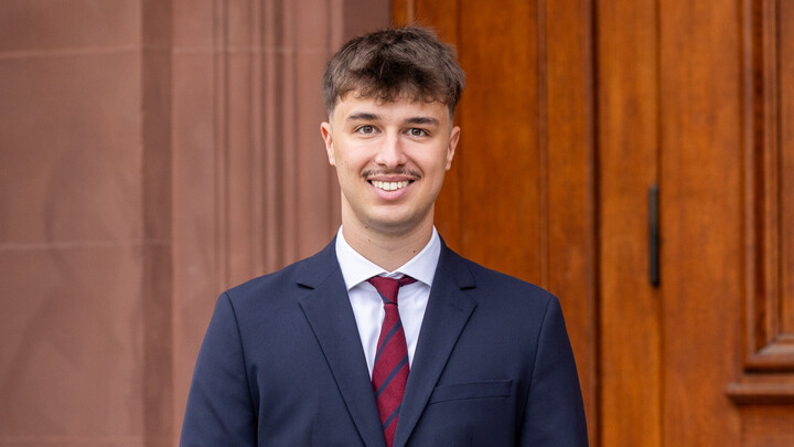 Ein Student im Anzug lächelt in die Kamera.