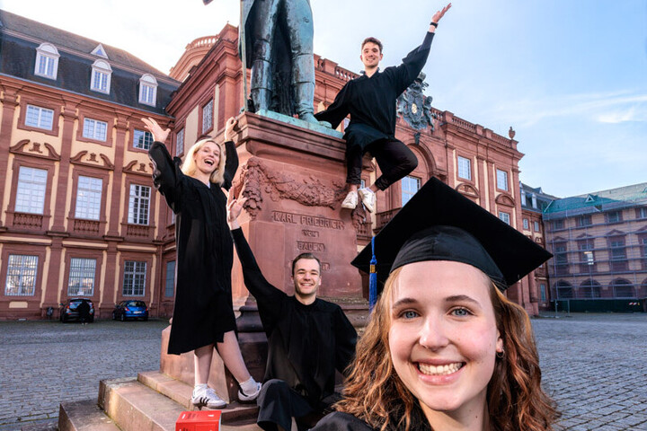Vier Studierende mit Roben und Hüten im Ehrenhof des Schlosses
