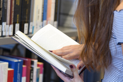 Nahaufnahme einer vor dem Buchregal stehenden Studentin, die in einem Buch liest.