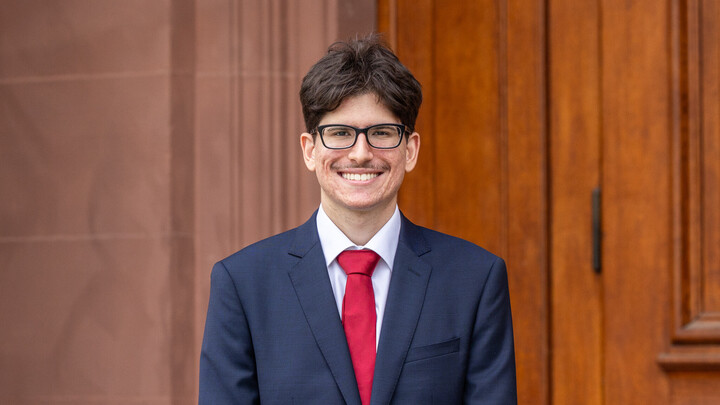 Ein Student im Anzug lächelt in die Kamera.
