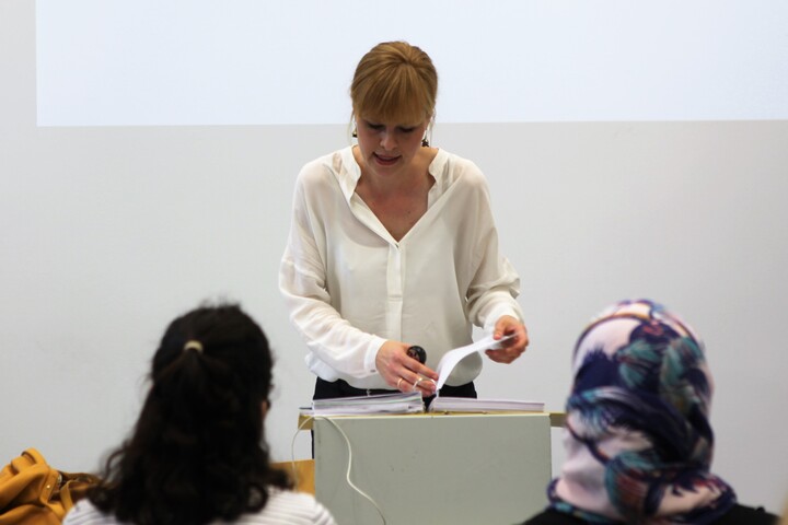 Lecturer speaking, with two students visible in the front row