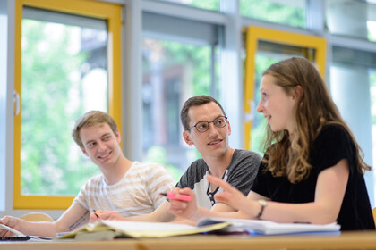 Drei Studierende unterhalten sich in einem Seminarraum.