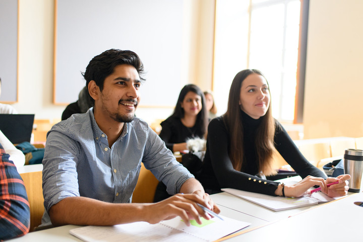 Zwei Studierende sitzen an einem Tisch und hören zu