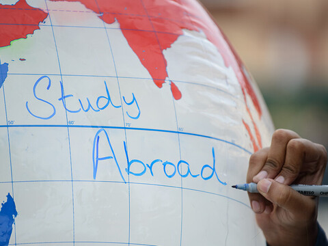 Eine Hand schreibt die Worte "study abroad" auf einen aufgeblasenen Globus.