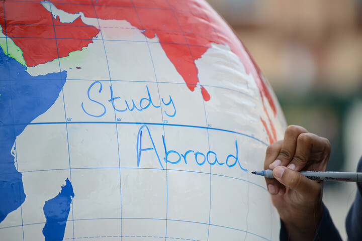 Eine Hand schreibt die Worte "Study Abroad" auf einen aufgeblasenen Globus