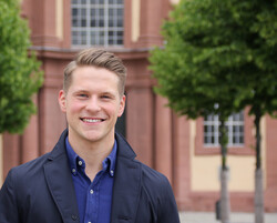 Johannes Harrack steht vor dem Schloss in blauem Hemd und Jacke