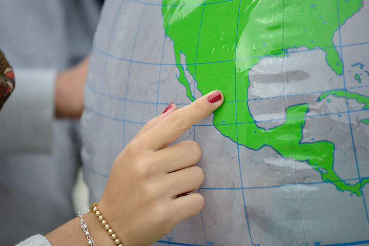 Eine Hand zeigt auf einen Ort auf einem Globus