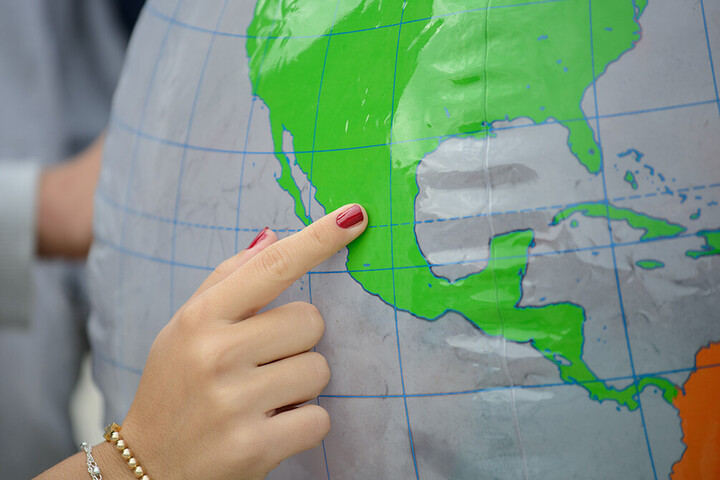 Eine Hand zeigt auf einen Ort auf einem Globus.