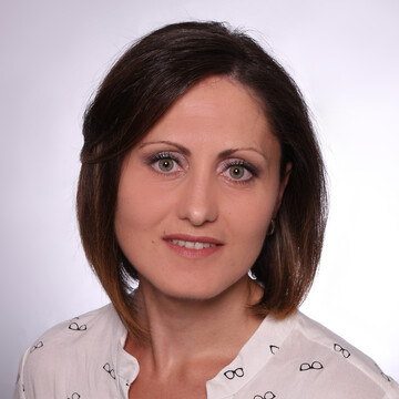 Milita Groß hat schulterlange, braune Haare und trägt eine weiße Bluse.