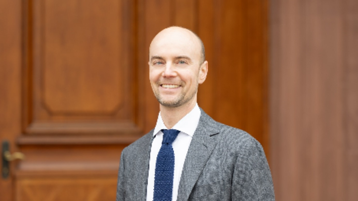 Porträt-Foto vor dem Schloss, Prof. Renner trägt Anzug und Krawatte und lächelt 