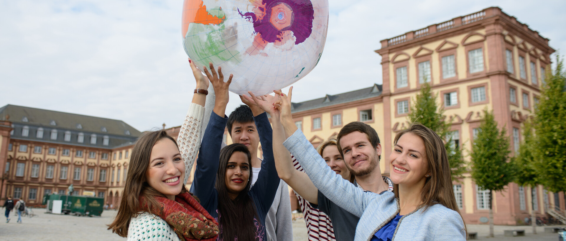 Eine Gruppe Studierender hält einen aufgeblasenen Globus vor dem Schloss in die Luft