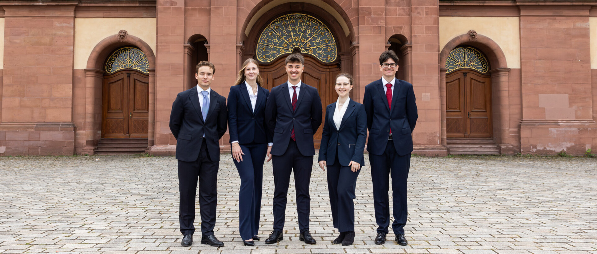 Fünf Studierende stehen in Anzügen vor der Universität Mannheim.