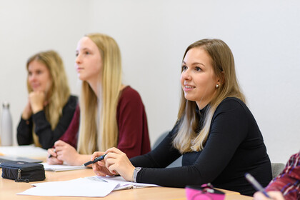 Drei Studentinnen sitzen nebeneinander in einem Seminarraum.