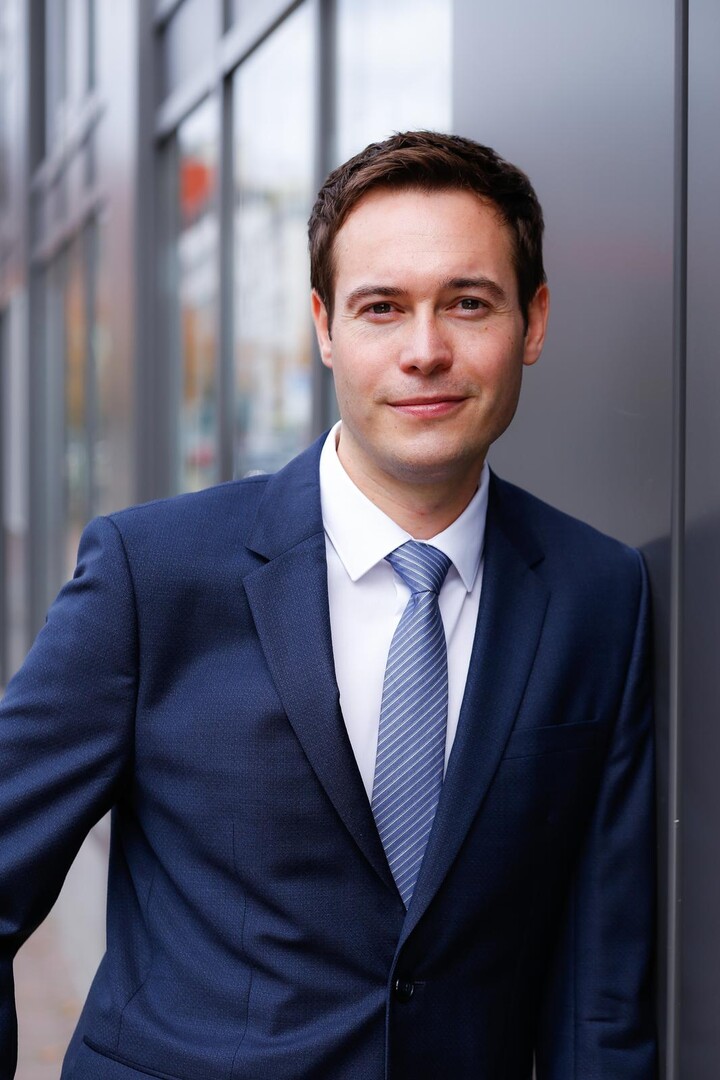 Mark Makowsky im Anzug an einer Wand anlehnend