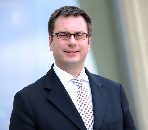 Andreas Maurer in black suit and tie smiling into camera