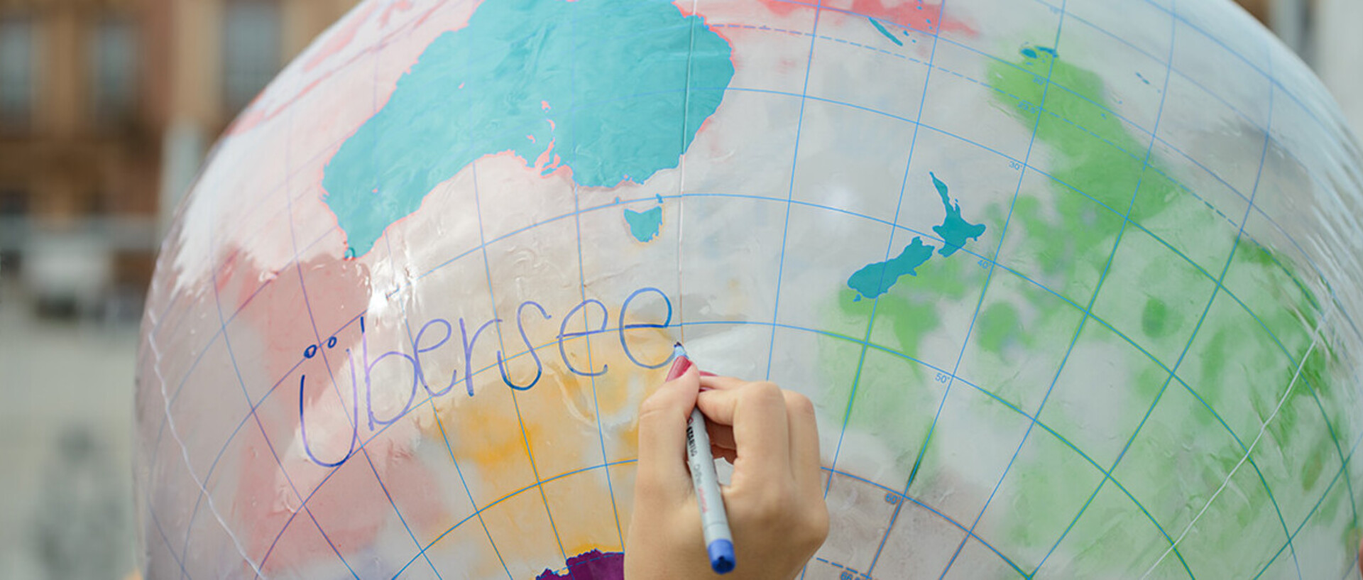 Eine Hand schreibt das Wort "Übersee" auf einen aufgeblasenen Globus