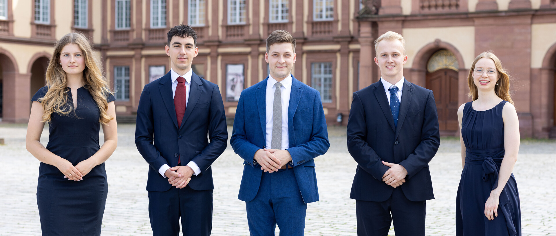Fünf Studierende stehen in Anzügen und Kleidern vor der Universität Mannheim.
