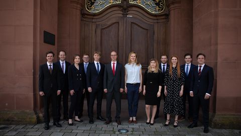 Eine Gruppe Studierender in Anzügen und Röcken vor dem Schloss