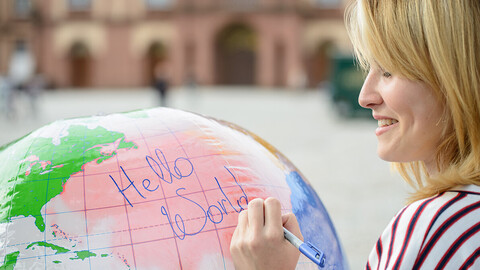 Eine Studentin schreibt die Worte "hello world" auf einen aufgeblasenen Globus
