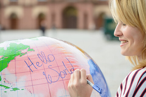 Eine Studentin schreibt die Worte "hello world" auf einen aufgeblasenen Globus