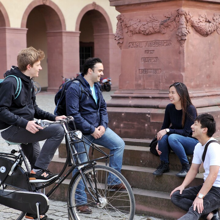 Eine Gruppe Studierender unterhält sich auf den Treppen einer Statue im Ehrenhof