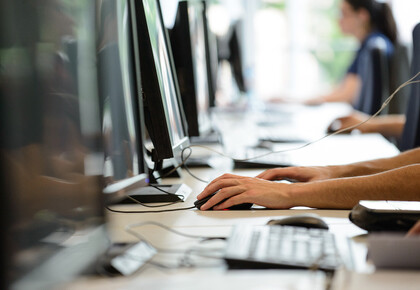 Vier Menschen sitzen in einer Reihe vor Computern.