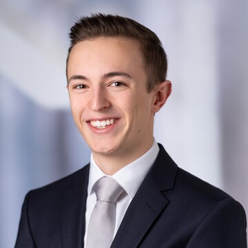 Porträt von Niklas Götz. Er trägt einen dunkelblauen Anzug, dazu ein weißes Hemd und eine silberne Krawatte.