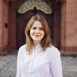 Annkathrin Wiltz lächelt und hat  hellbraunes und schulterlanges Haar. Sie trägt eine weiße Bluse mit goldenen Punken.