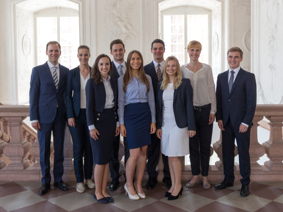 Gruppe von Studierender in formeller Kleidung vor den Fenstern eines Raumes