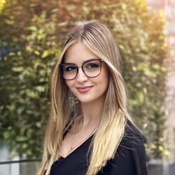 Blonde Frau mit Brille vor einem Baum mit bunten Blättern
