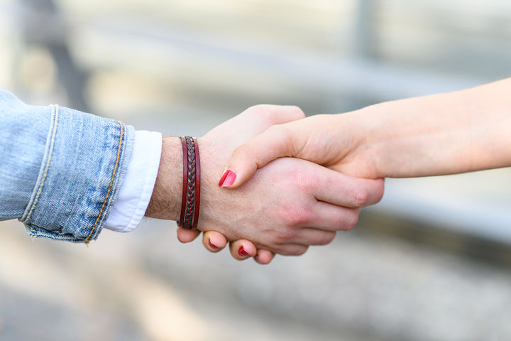 Ein Händedruck. Eine der Hände hat ein Lederarmband am Arm, die andere trägt Nagellack.