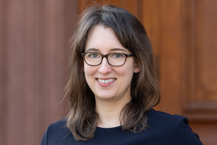Portrait von Professorin Stefanie Egidy. Sie trägt ein schwarzes Oberteil und steht vor einer brauen Tür der Universität.