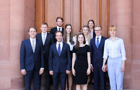 Eine Gruppe Studierender in Anzügen und Kleidern vor dem Schloss