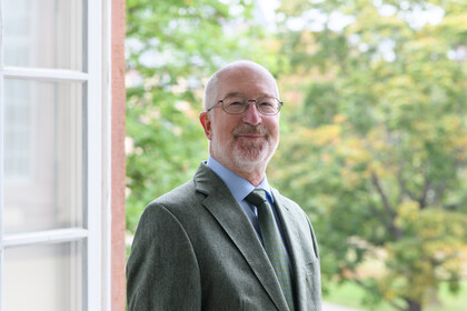 Portrait von Jochen Taupitz. Er trägt einen grünen Anzug und steht lächelnd vor einem Fenster.