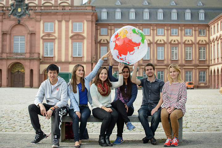 Studierende sitzen auf Bank im Ehrenhof und halten einen aufgeblasenen Globus in die Luft
