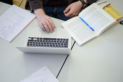 Ein Student sitzt mit Büchern und seinem Laptop an einem Tisch.