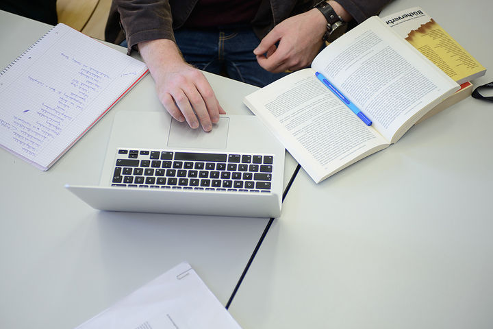 Ein Student sitzt mit Büchern und seinem Laptop an einem Tisch.