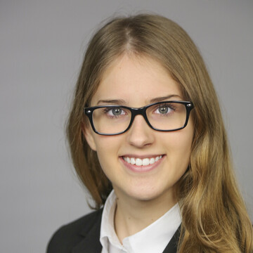 Laura Mikschy hat lange hellbraune Haare. Sie trägt eine dunkle Brille, ein weißes Hemd und einen schwarzen Blazer.