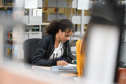Eine Studentin in der Bibliothek schreibt am Laptop
