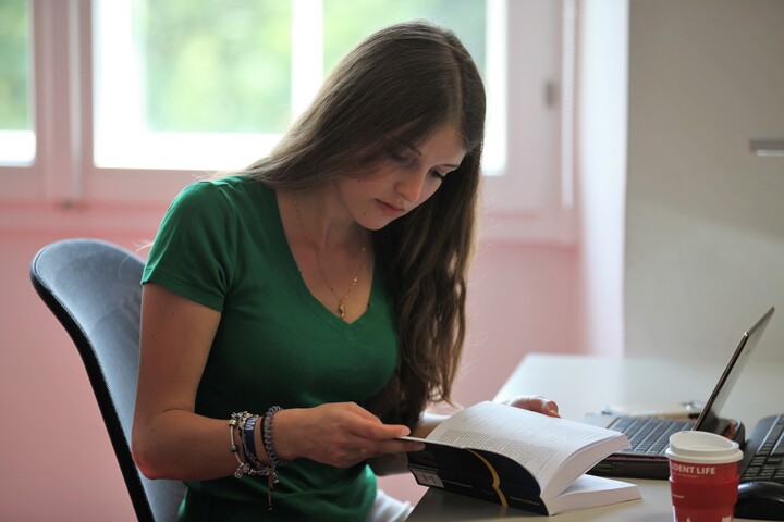 Studentin sitzt an einem Tisch und liest